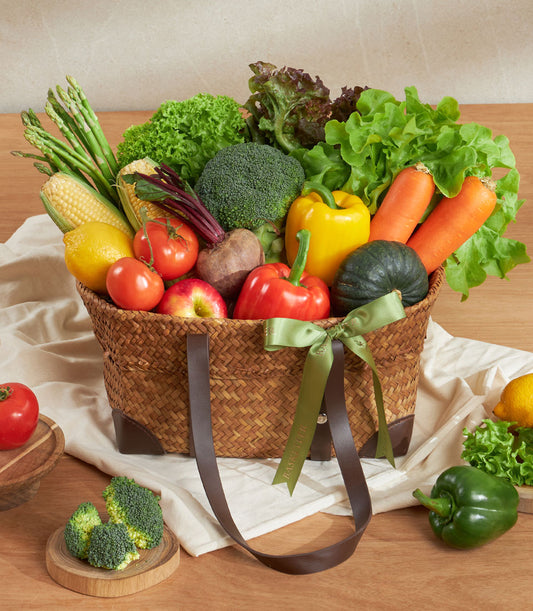 Woven straw basket filled with fresh farm vegetables and fruits, tied with green ribbon bow
