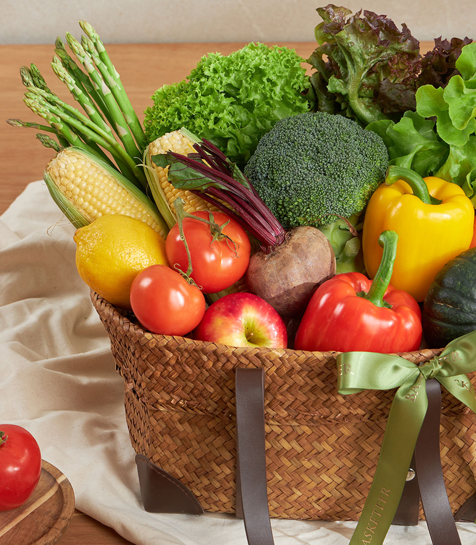 Fresh farm vegetable basket with asparagus, corn, tomatoes, and greens in woven natural fiber basket