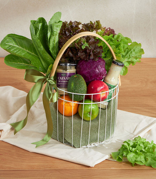 Green wellness vegetable basket with fresh lettuce, cabbage, apples, oranges, avocado and gourmet dressing