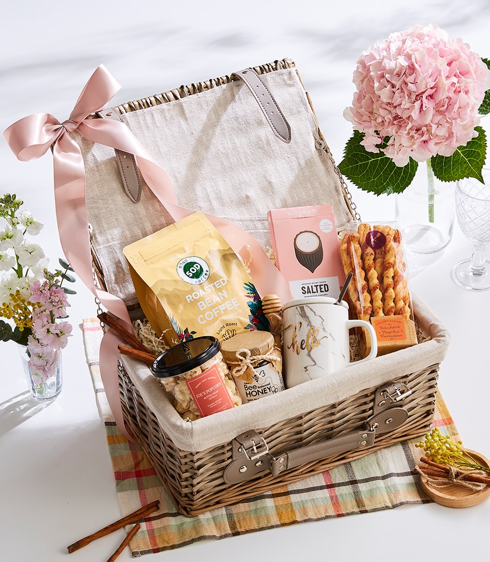 Light wicker picnic basket with gourmet coffee, caramel, honey, popcorn, breadsticks, and ceramic mug on plaid tablecloth