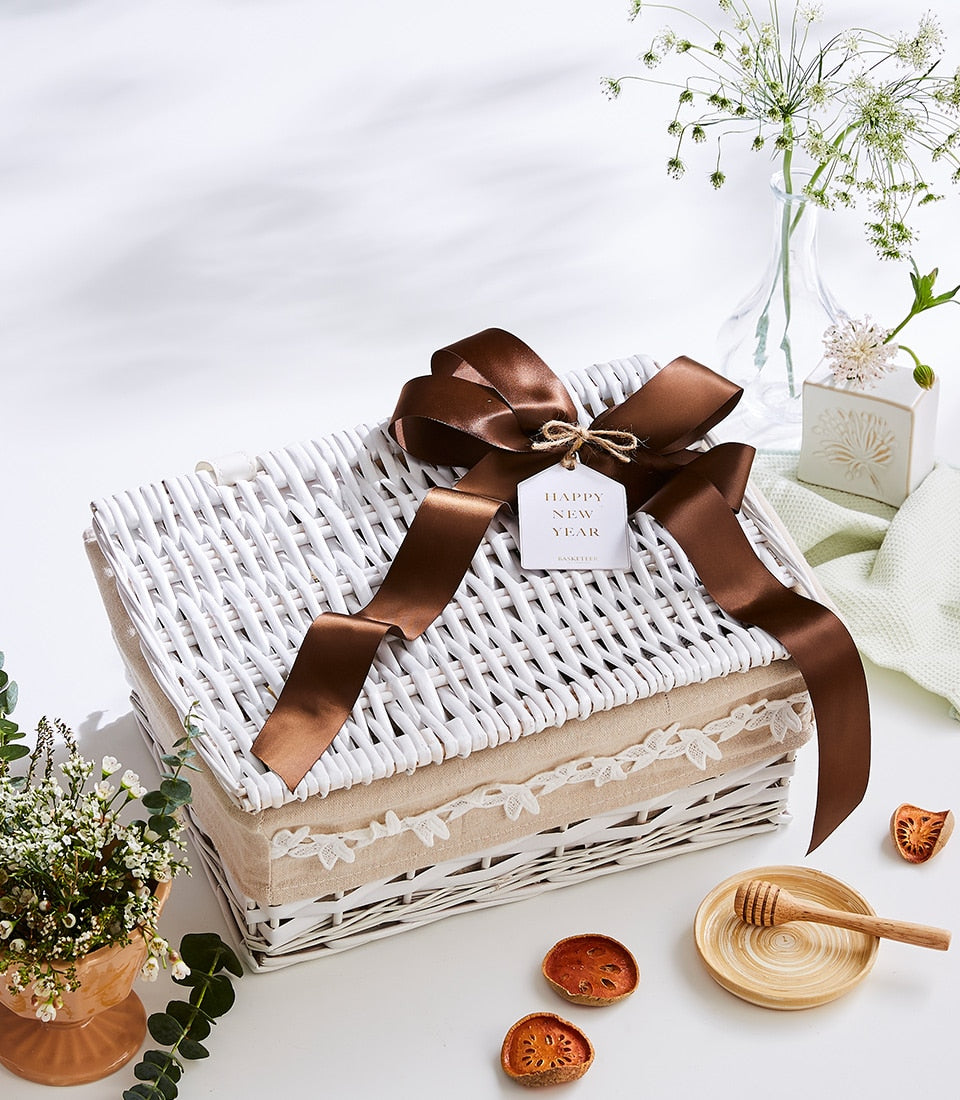 White wicker hamper with brown satin bow and lace-trimmed linen lining, styled with fresh flowers and gourmet picnic
