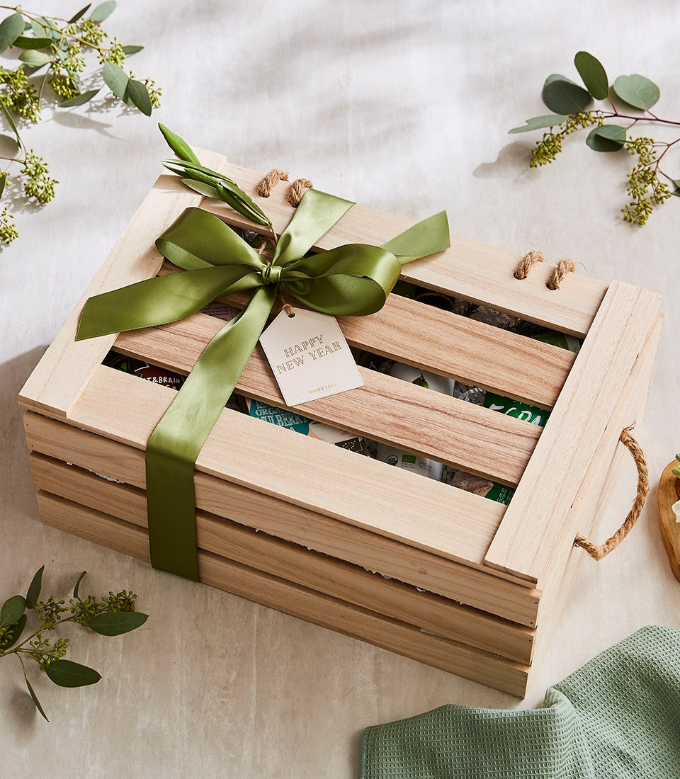 Wooden crate gift box with green satin bow filled with organic wellness snacks and health foods