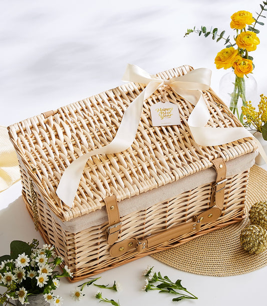 Wicker picnic basket with beige lining, cream satin bow, and Happy New Year gift tag, surrounded by yellow flowers and gold