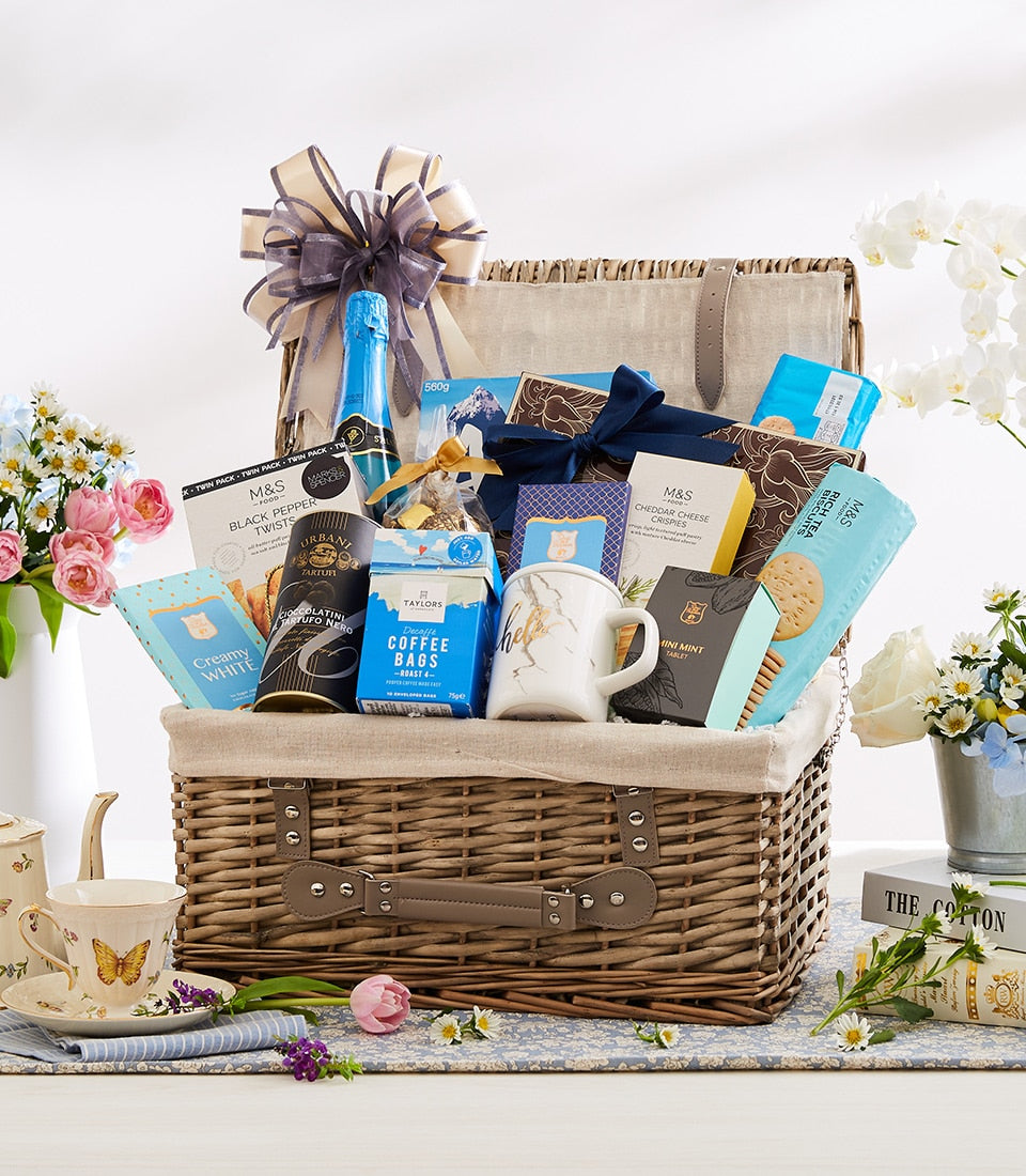 Wicker gourmet hamper with sparkling beverage, biscuits, chocolate, coffee and marble mug tied with grey ribbon