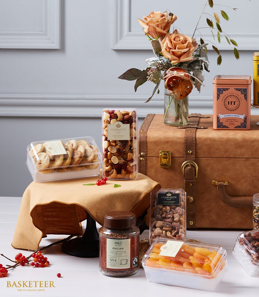 Luxury gift hamper with peach roses, gourmet cookies, nuts, dried fruit, and specialty coffee in brown leather trunk display