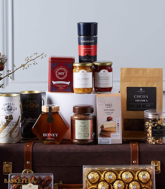 Luxury gourmet hamper with coffee, tea, preserves, and artisan treats arranged on dark leather trunk