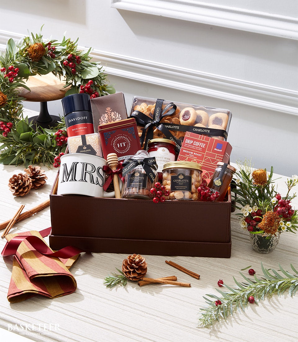 Luxury gourmet gift box with coffee, tea, honey, and Charlotte bakery treats, surrounded by festive greenery and red flowers
