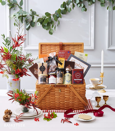 Wicker picnic basket filled with gourmet chocolates, nuts, coffee, and biscuits, styled with fresh flowers and festive table