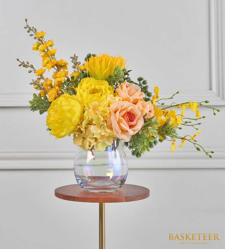 Yellow peony and hydrangea artificial flower arrangement in iridescent glass vase on gold stand
