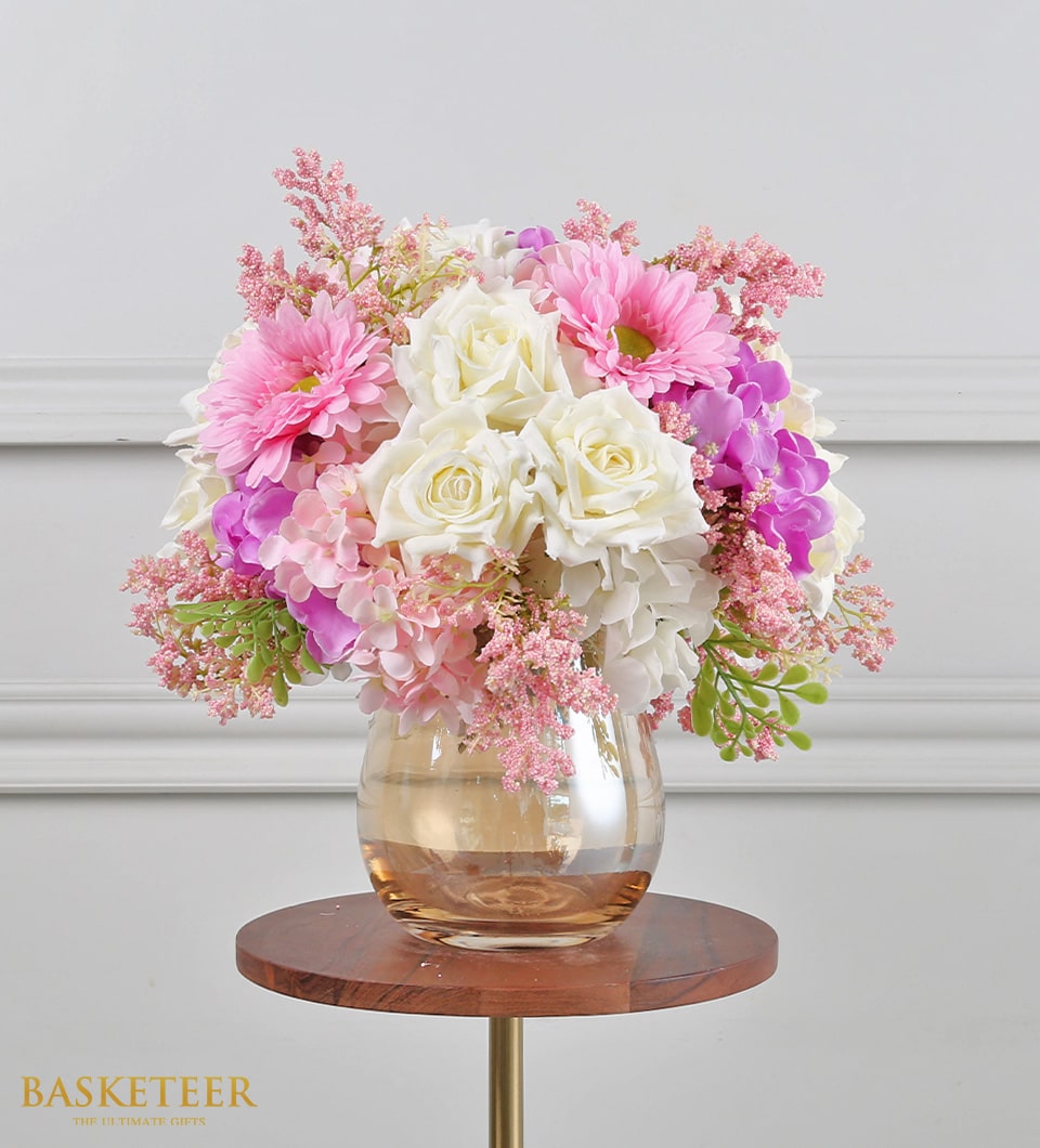 Bright artificial flower arrangement with white roses and pink gerberas in amber glass vase