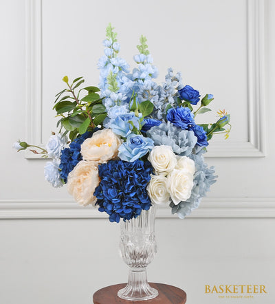 Elegant blue-toned artificial flower arrangement with roses, hydrangeas, and delphiniums in glass vase