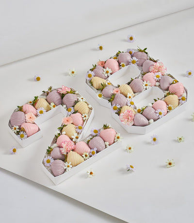 Chocolate-dipped strawberry number box "29" with pastel pink, yellow, and lavender coating, fresh flowers, and foliage for