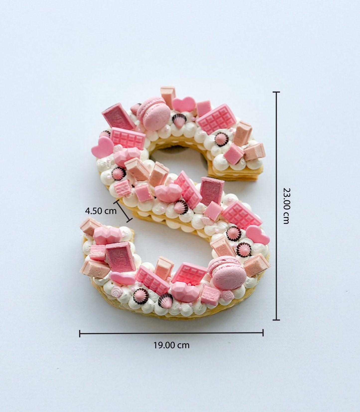 Pink "S" letter cake with cream rosettes, macarons, and candy toppings for birthdays
