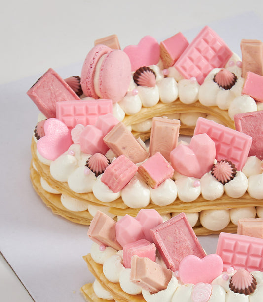 Heart-shaped pink puff letter cake with cream, macarons, and pink chocolates from Charlotte Bakery
