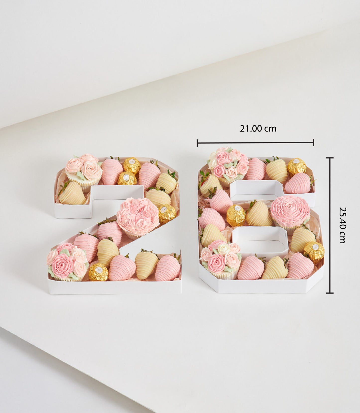 White number-shaped gift boxes filled with chocolate-dipped strawberries, Ferrero Rocher, and pink frosted cupcakes for