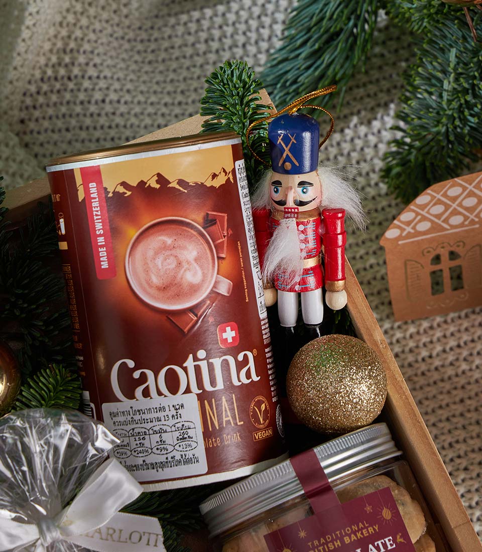 Festive Christmas gift box with Swiss hot chocolate, British bakery cookies, wooden nutcracker, and gold ornaments on