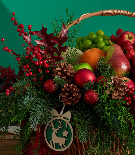 Luxury wicker Christmas fruit basket with fresh grapes, apples, pears, strawberries, evergreen branches and festive red