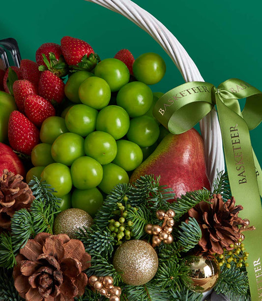 Christmas white wicker basket filled with fresh strawberries, pears, grapes, and evergreen pine branches with gold