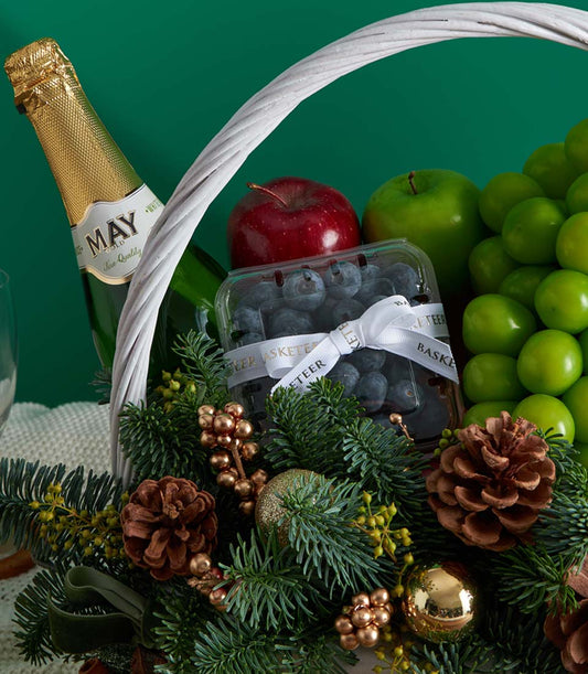 Premium Christmas fruit basket with sparkling wine, fresh apples, grapes, and blueberries, festive evergreen and gold