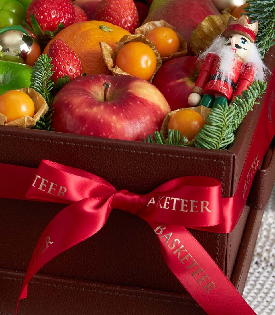 Festive Christmas fruit basket with red apples, tangerines, strawberries, and physalis, green fir branches, nutcracker