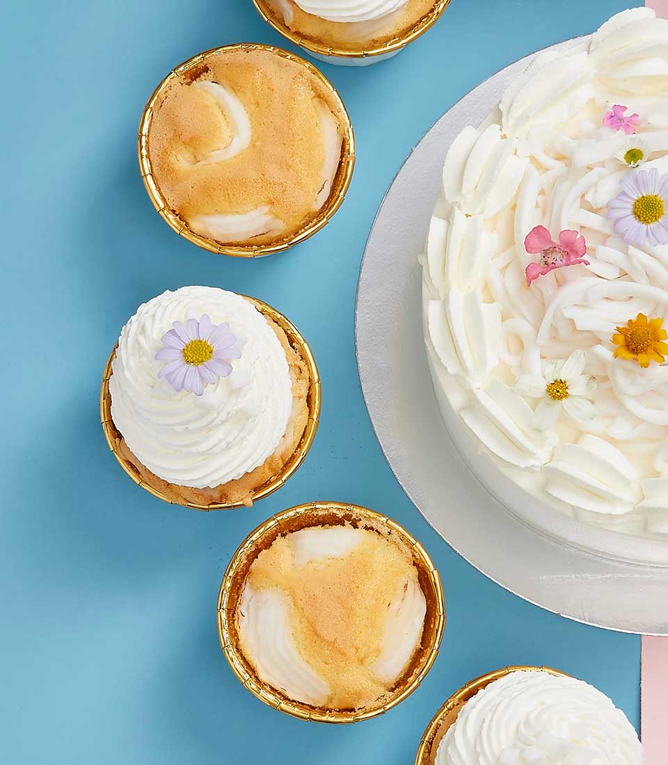 Coconut celebration cake with cupcakes, white cream frosting, fresh flowers, and shredded coconut for Mother's Day
