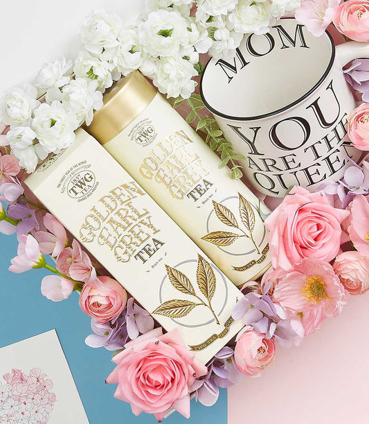 Luxurious Mother's Day gift set with Golden Earl Grey Tea, queen mug, and fresh white ranunculus and pink roses