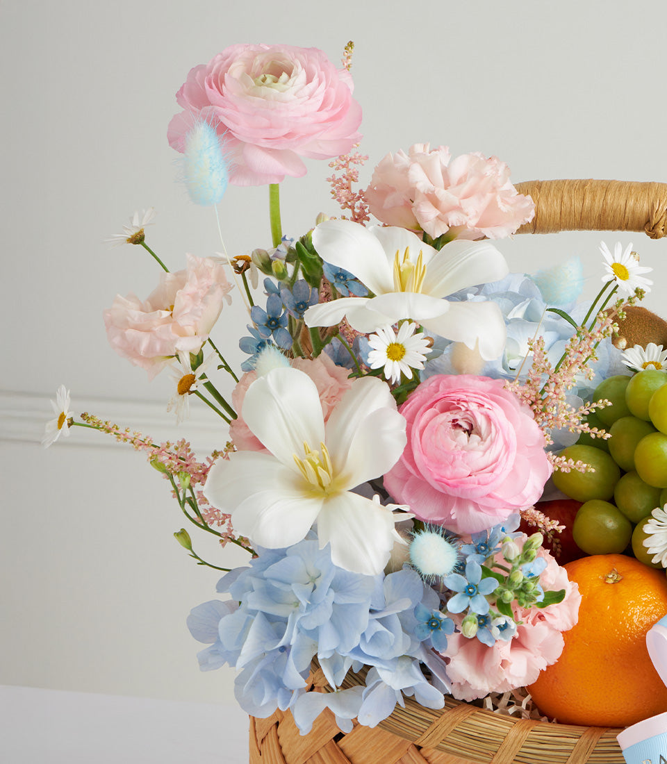 Pastel fruit basket with pink, white and blue flowers, fresh grapes and oranges for Mother's Day
