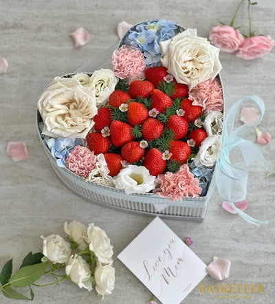 Heart-shaped gift box with fresh strawberries, white roses, and hydrangeas in light blue striped packaging with ribbon