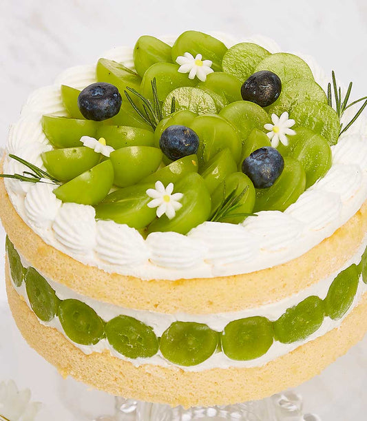 Two-tier grape and blueberry birthday cake with fresh berries, edible flowers, and rosemary on cream-filled sponge