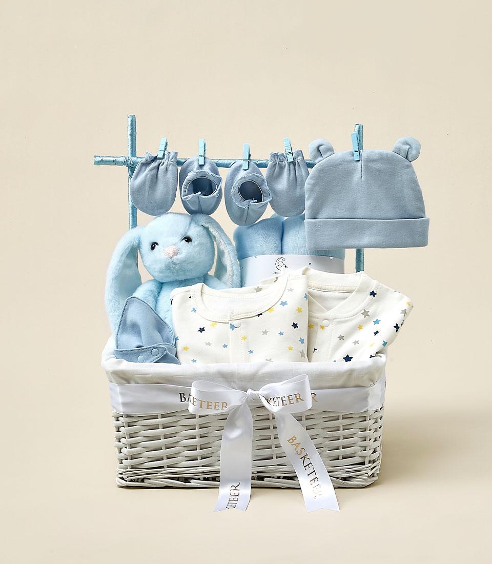 Blue and white woven baby gift basket with plush bunny, star bodysuits, hat, mittens and booties