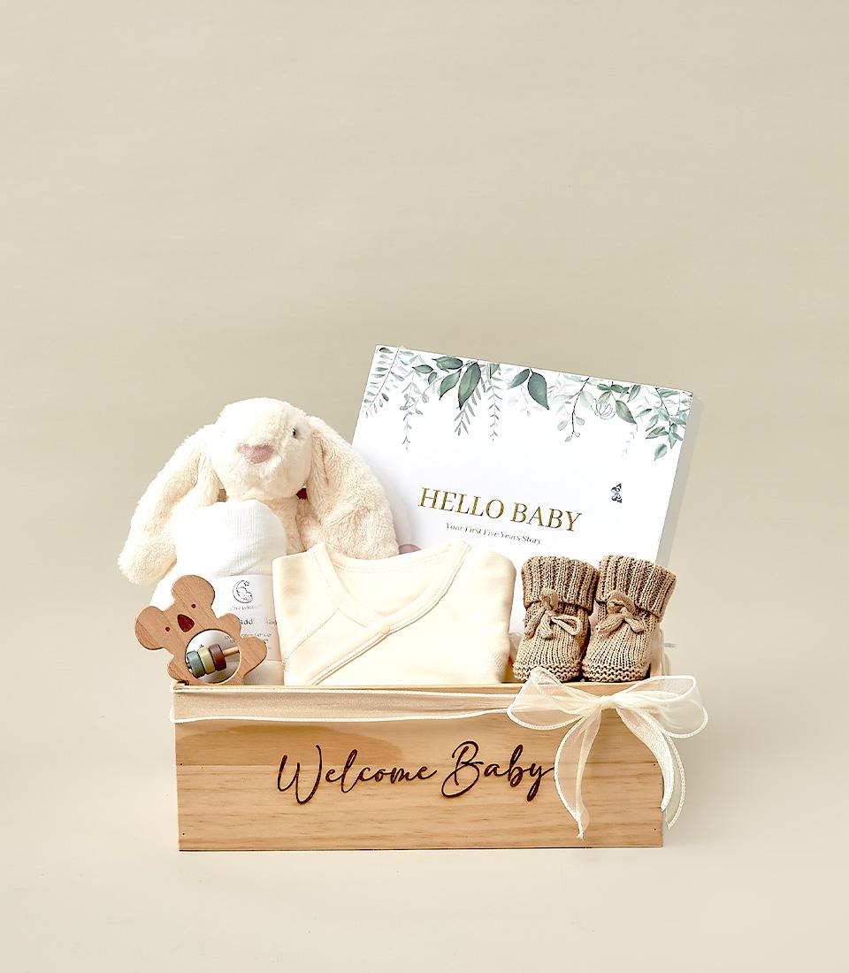 Welcome Baby wooden box gift set with plush bunny, white swaddle, bear rattle, cream onesie, brown booties and memory book