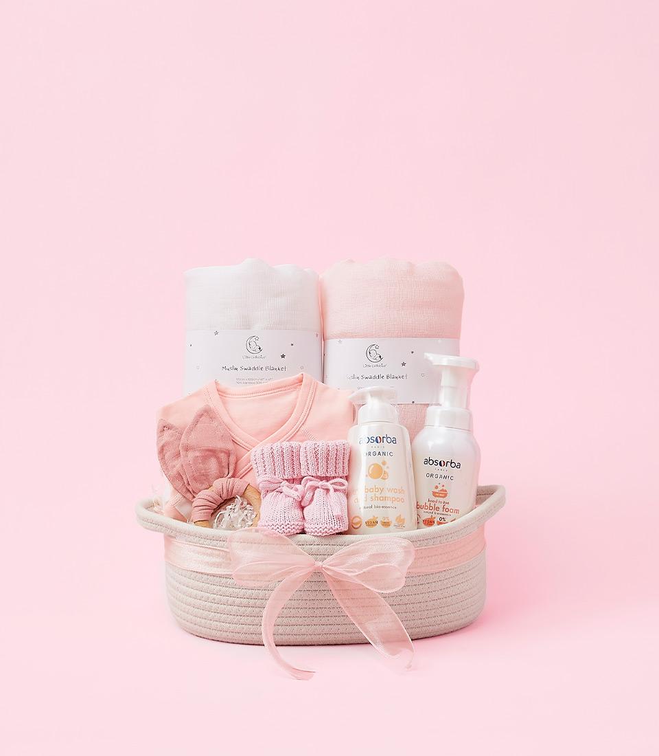 Woven pink and white baby gift basket with muslin swaddles, organic wash, wooden teether, and booties