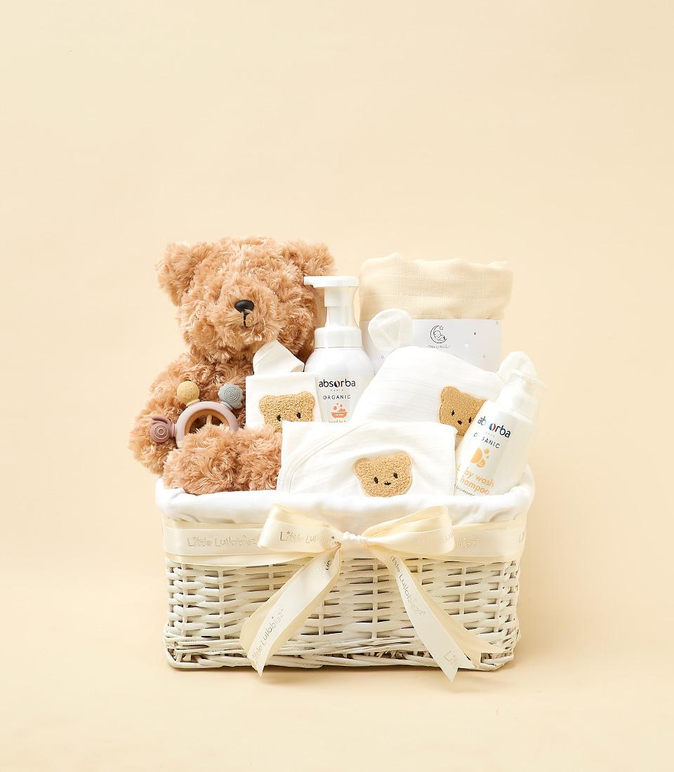 Happy Bunny Soft Bliss baby gift basket with teddy bear, organic wash products, and white cotton pieces in woven wicker