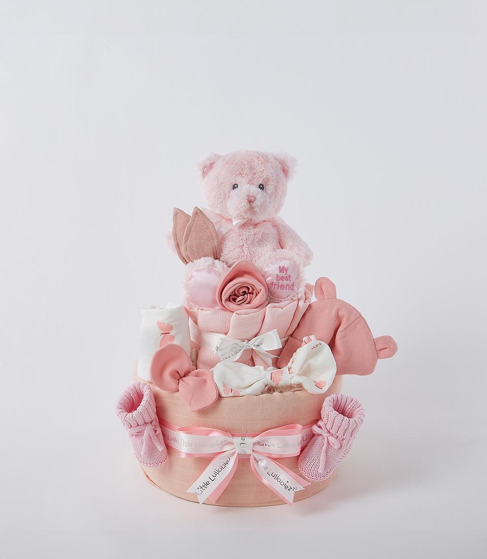 Two-tier pink diaper cake with baby booties, teddy bear, and folded essentials for newborn gifting