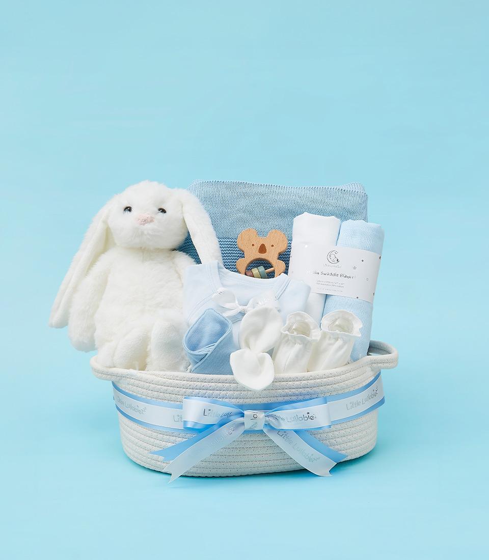 White woven baby gift basket with bunny plush, knit blanket, and newborn essentials in soft blues