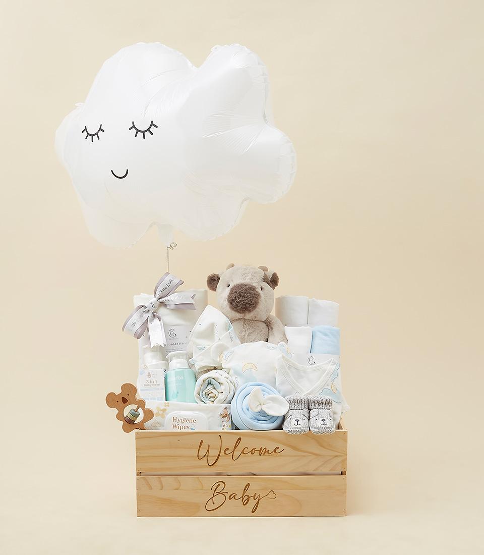 Welcome Baby gift hamper with plush toy, booties, clothing, care essentials, and cloud balloon in wooden crate