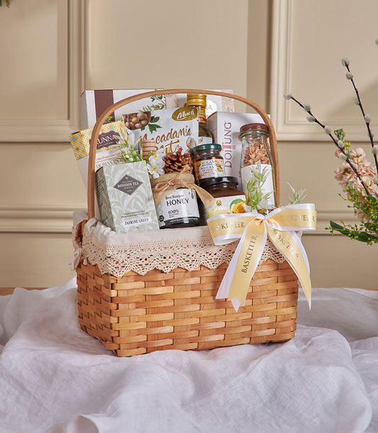 Premium wicker gift basket with jasmine tea, manuka honey, macadamia nuts, and wellness treats tied with yellow ribbon