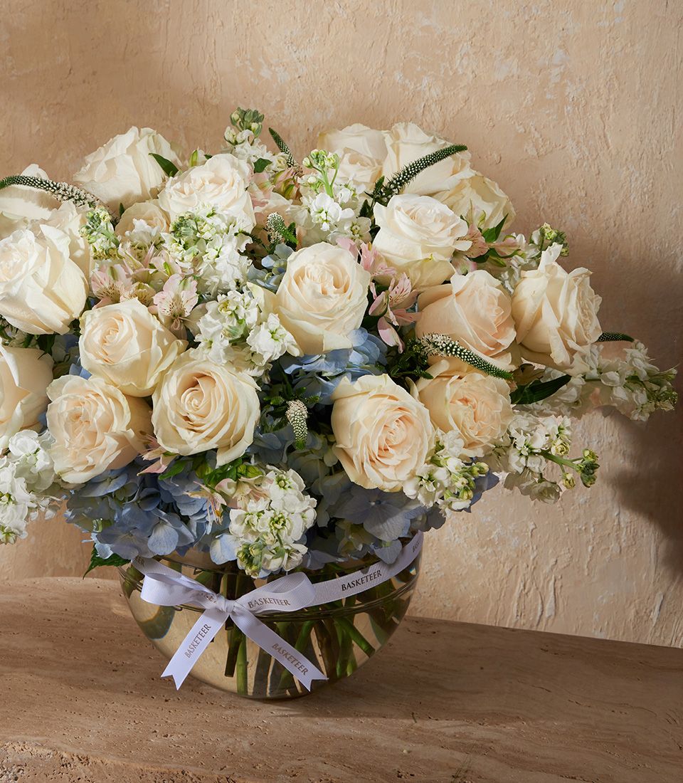 Cream and peach roses with white stock and light blue hydrangeas in elegant clear glass bowl arrangement