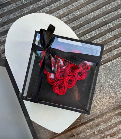 Black gift box with heart-shaped arrangement of preserved red roses and satin ribbon bow