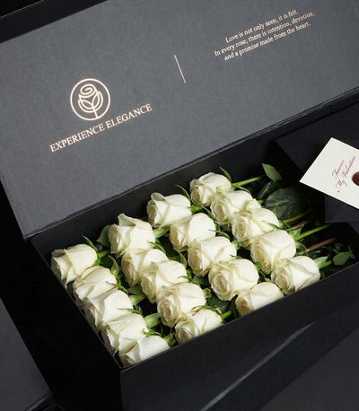 Luxury white rose bouquet in dark matte gift box with gold-foil logo and Valentine's Day message card