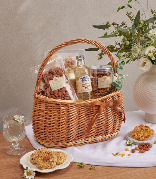 Woven wicker basket of premium almond cookies, roasted nuts, and ginger ale with artisan baked goods
