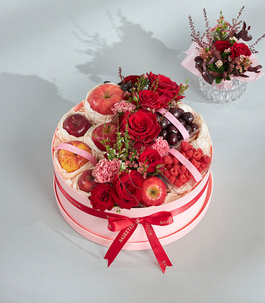 Round luxury gift box with red roses, fresh apples, cherries, raspberries, and pink carnations for birthday gifting