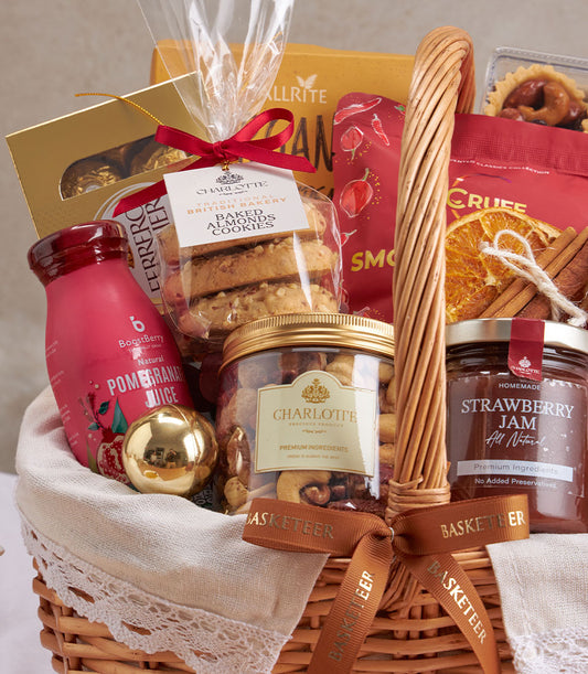 Light brown wicker gift basket with gourmet tea, artisan cookies, mixed nuts, chocolates, and festive dried fruit garnish