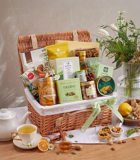 Premium wellness gift basket with gourmet foods, teas, honey, and artisan treats in wicker with green ribbon