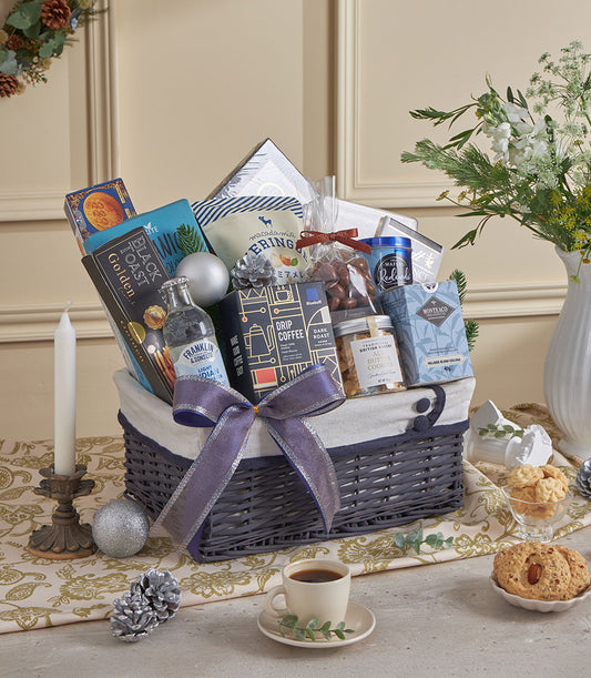 Luxury grey wicker gift basket with purple ribbon, filled with gourmet coffee, cookies, tea, and nuts for New Year