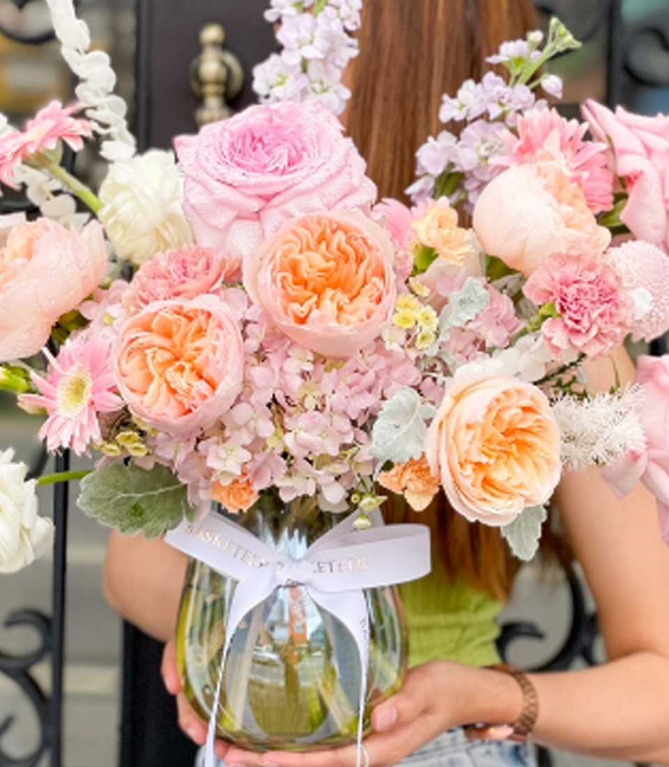 Elegant flower arrangement from Flowers by Basketeer with pink roses, peach David Austin roses, and hydrangeas in a glass vase tied with a white ribbon. Premium flowers for flower delivery Bangkok.