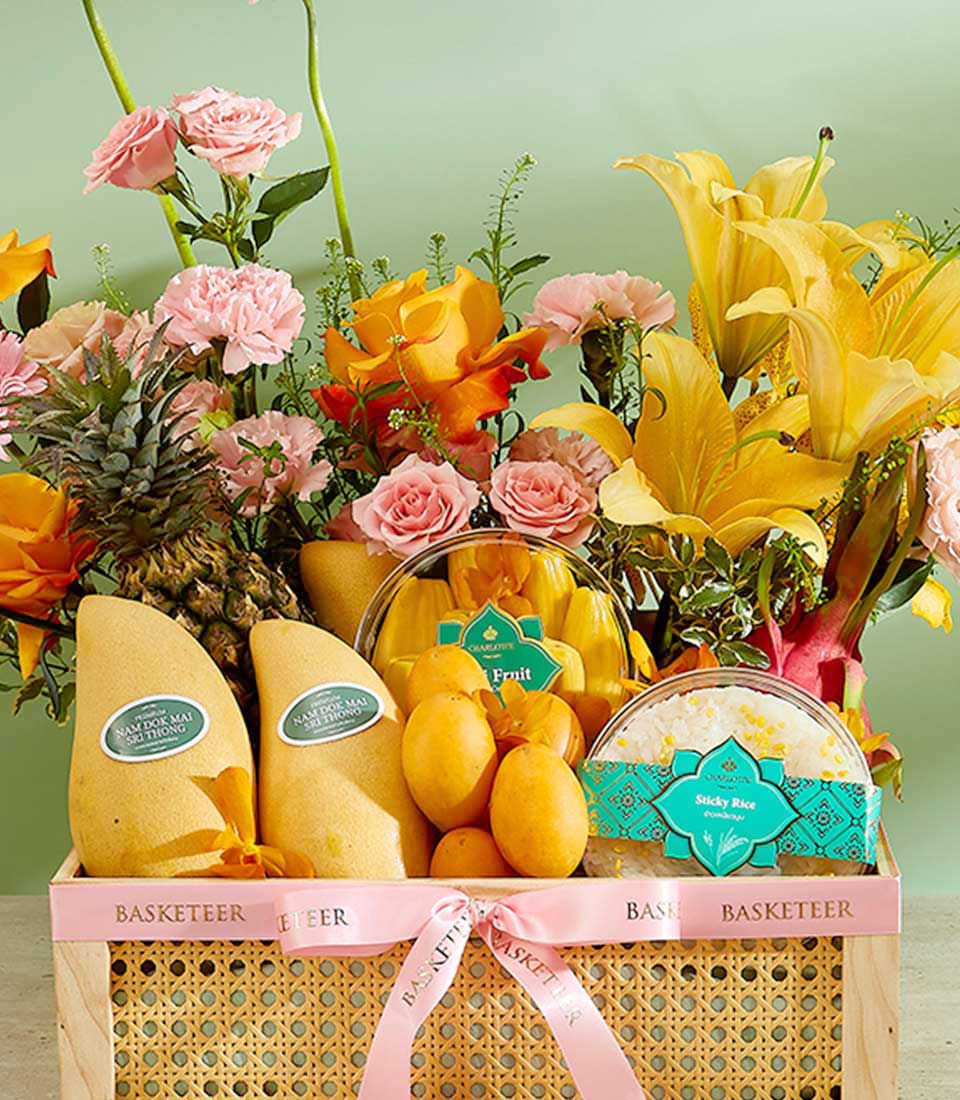 Tropical fruit gift basket with mangoes, pineapple, sticky rice, and yellow lilies with pink roses