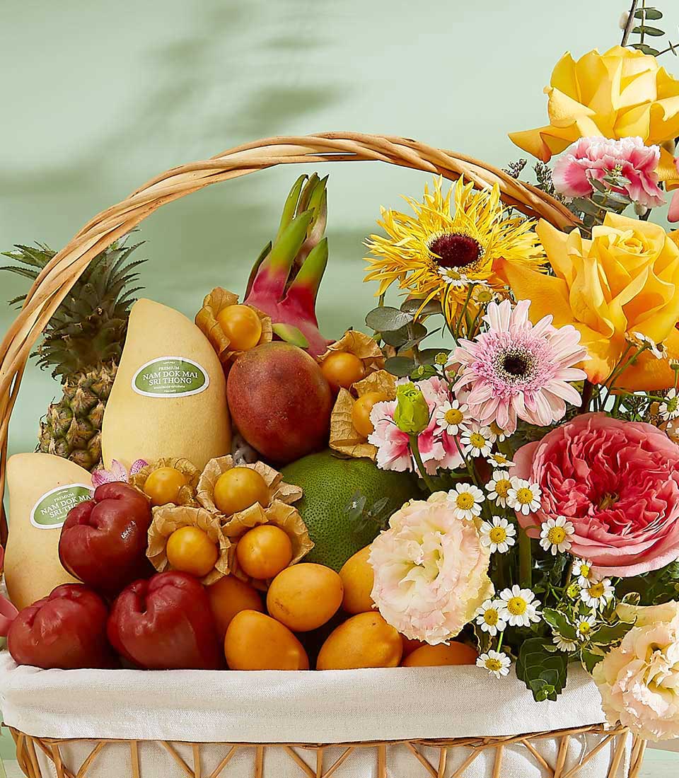 Tropical fruit and flower gift basket with premium mangoes, dragon fruit, roses, and sunflowers in woven wicker