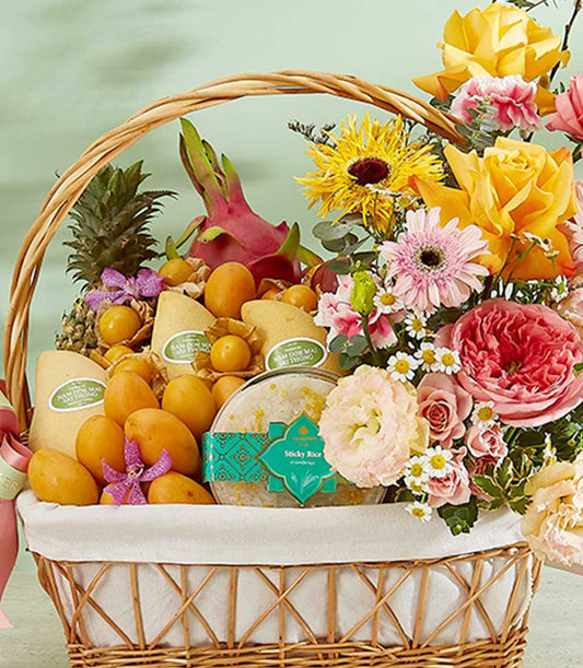 Woven wicker hamper with fresh Thai mangoes, pineapple, dragon fruit, and seasonal tropicals, paired with yellow roses and