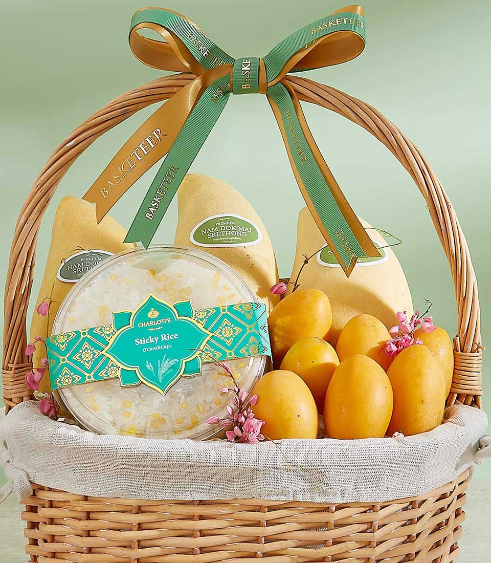 Woven wicker gift basket with premium Thai mangoes, sticky rice, and pink flowers tied with gold and green Basketeer ribbons